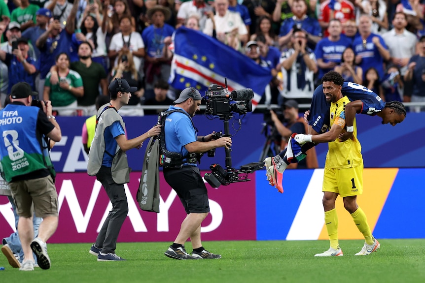 A goalkeeper lifts a teammate over his shoulders in celebration.