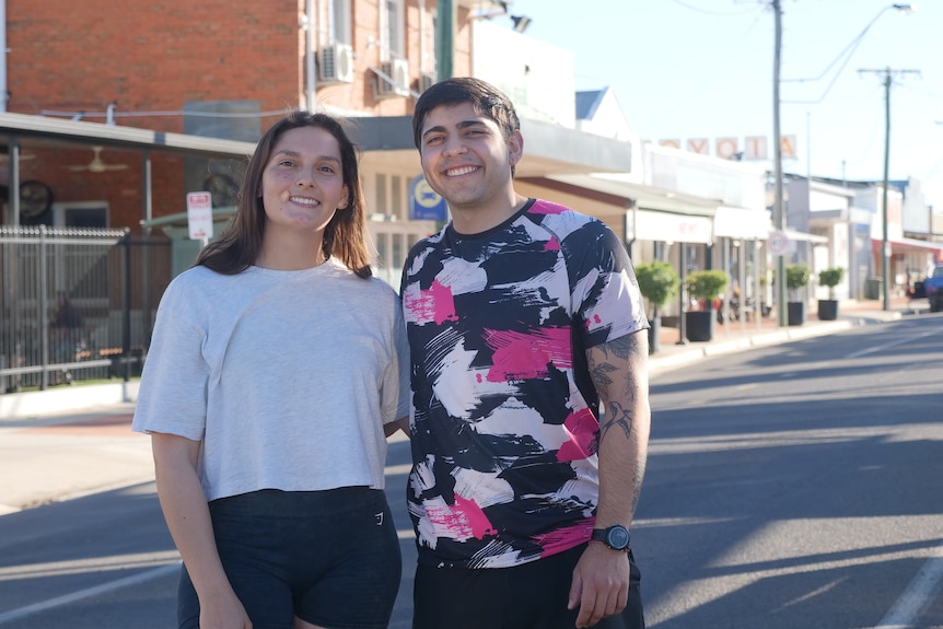 two backpackers standing in an outback town street smiling at the camera