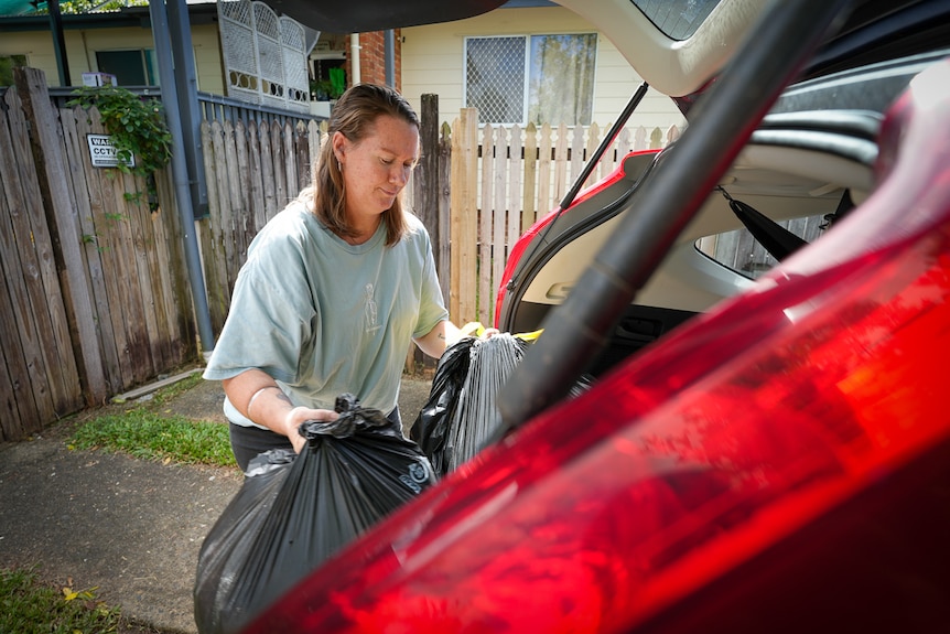 A woman loading her car with two full garbage bags.