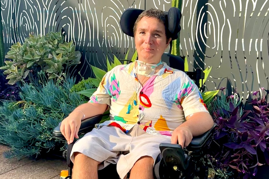 A man in a colourful shirt sitting in a wheelchair near a garden bed