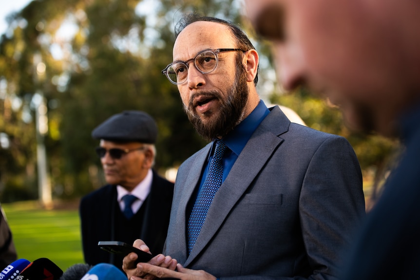 Abdullah Khan speaking in front of microphones.
