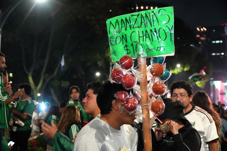 A man holds a pole with toffee apples sticking out.