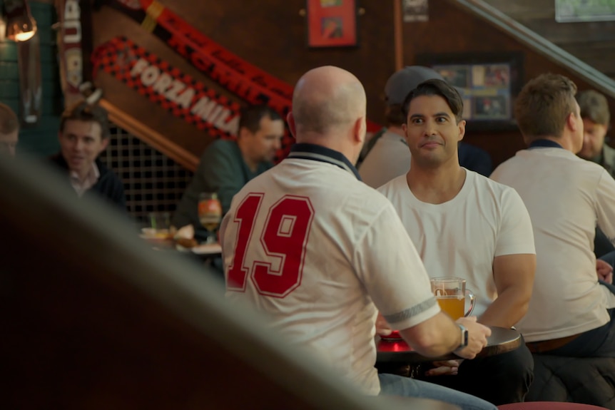 Marc, right, sits with wide eyes next to a man at a bistro table at a pub while they share beers.