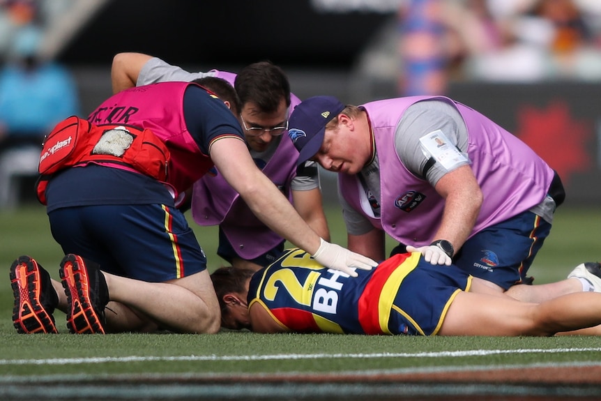 An Adelaide Crows AFLW player lies on the ground and is attended to by medical staff after being concussed.