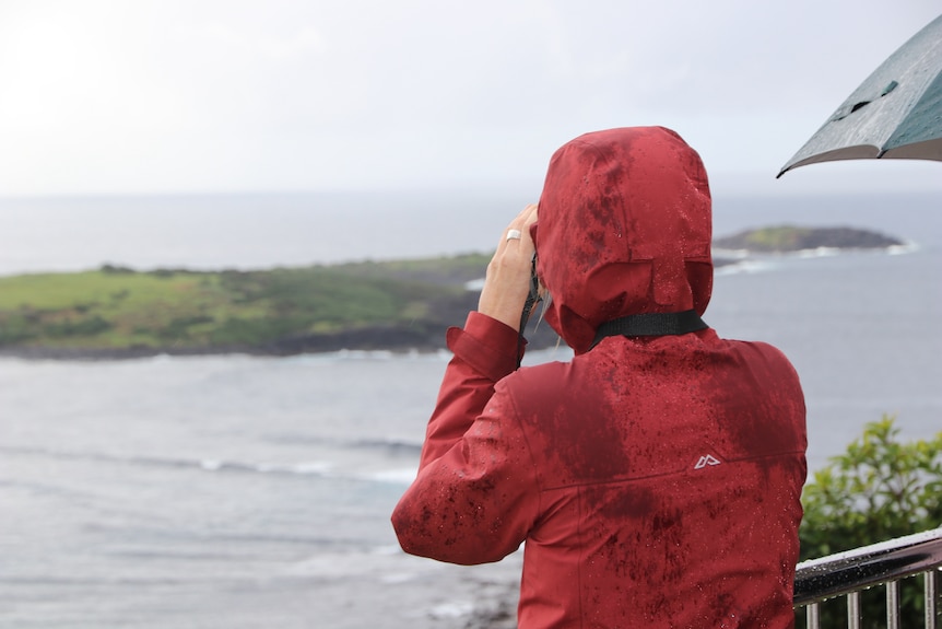 A volunteer in a red rain jacket watches the coast with binoculars