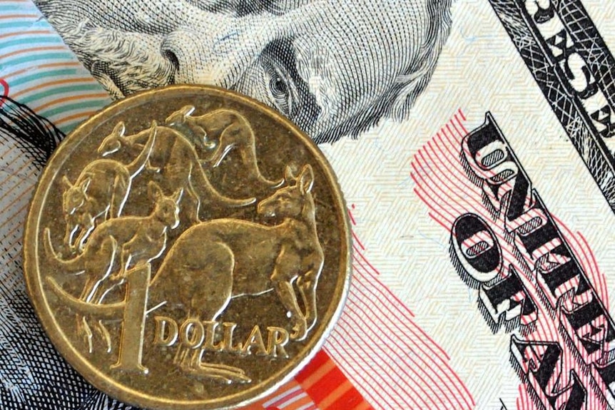 An Australian dollar coin placed on a US bank note.