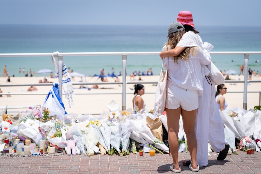 People hug at floral tribute Bondi Beach promenade