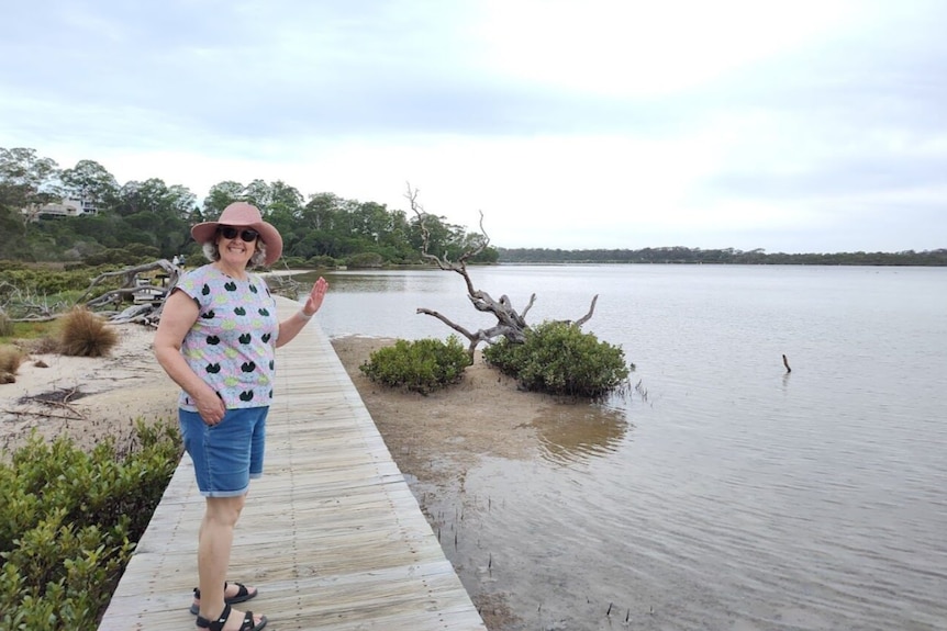 A woman stands on a boardwalk gesturing with her hands.