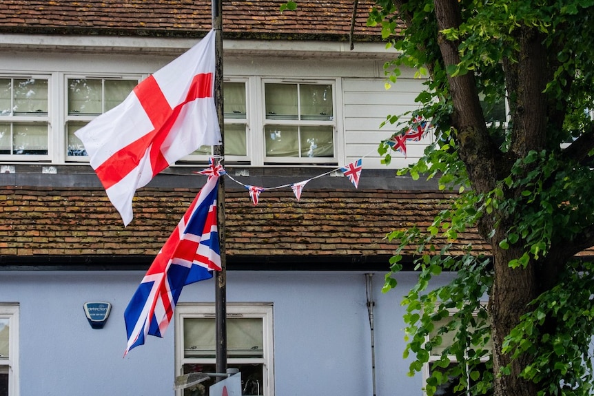 Two flag flying near a building.