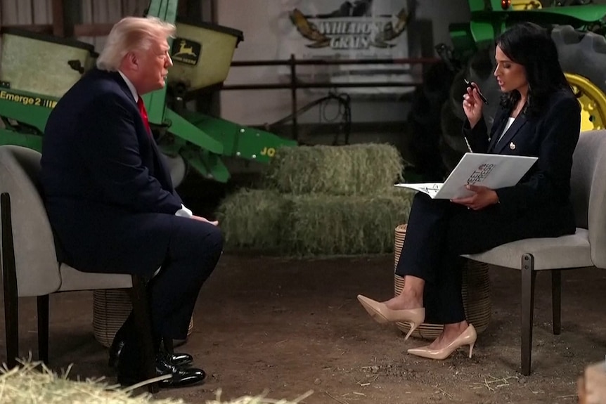 A man — Donald Trump — and a dark-haired woman sit in a barn, facing each other for an interview.