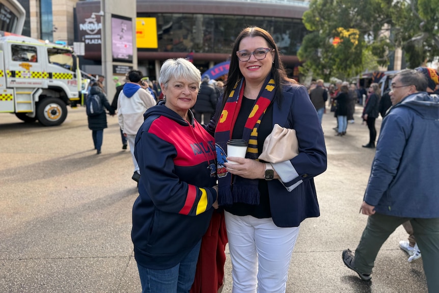 Two women wearing Crows fan gear in a forecourt