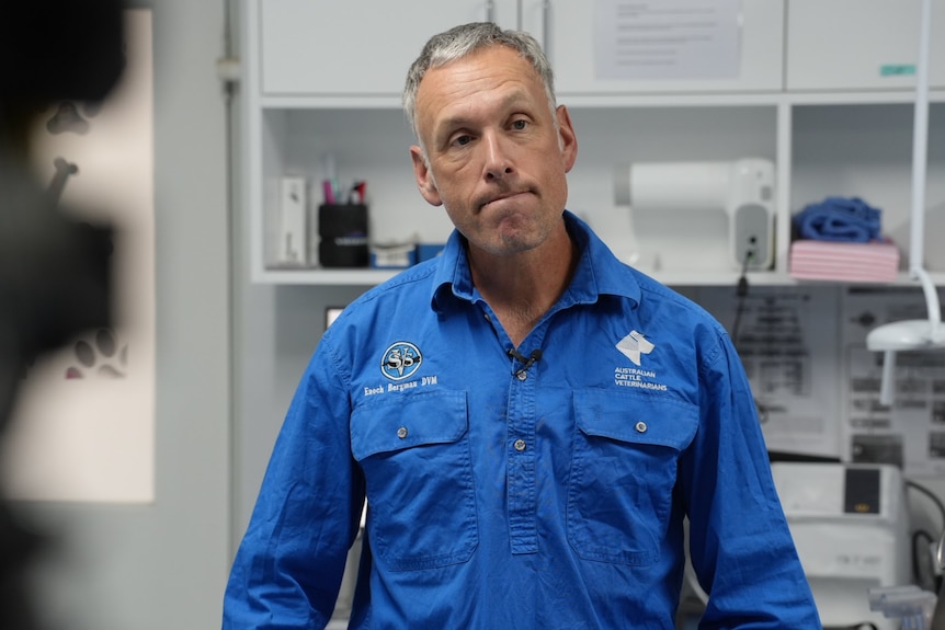 a man in a blue collared shirt looks dis-pleased, standing in a vet practice