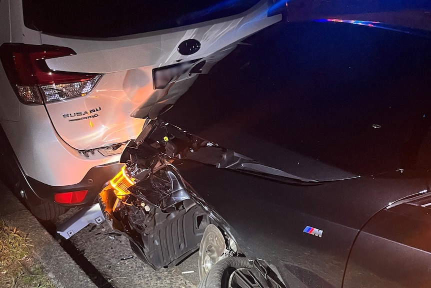 The crumpled bonnet of a black BMW pushed up against the crumpled back of a white Subaru.