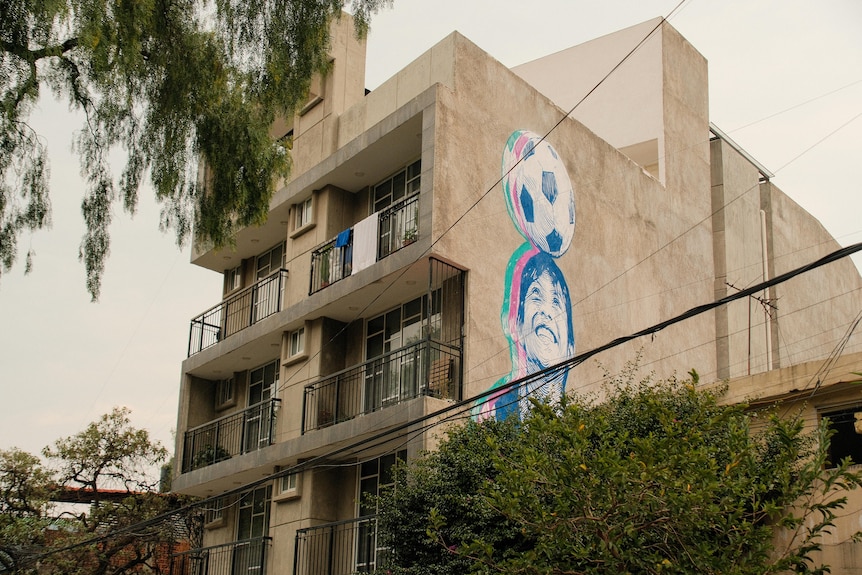 A mural of a boy headbutting a soccer ball on the side of an apartment building.