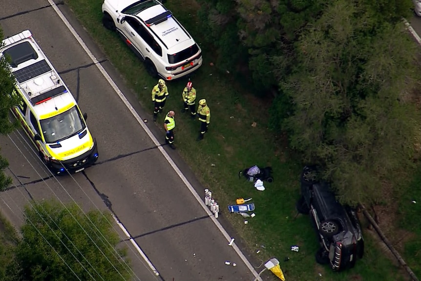 An aerial image showing an ambulance and police car parked near a dark car flipped on its side.