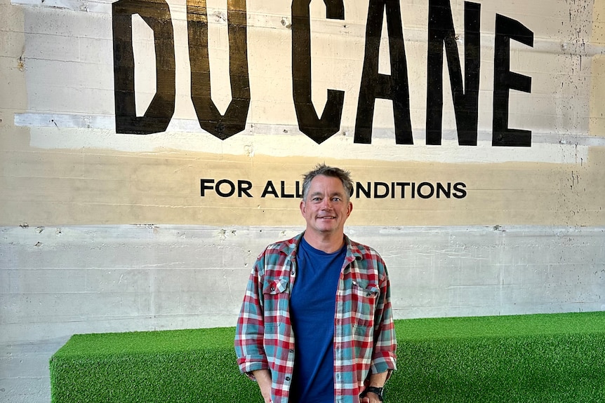 A man in flannel standing slightly smiling