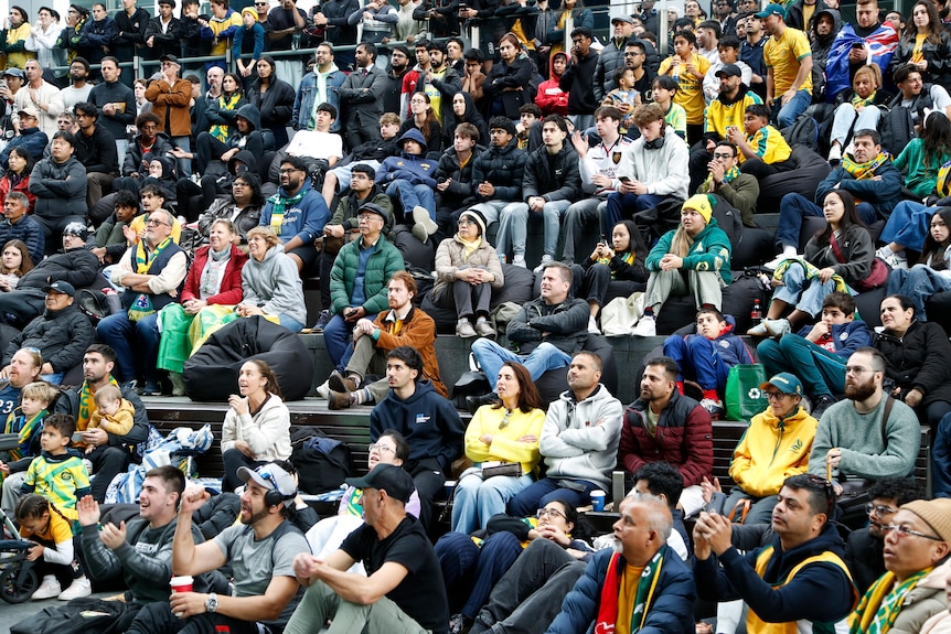A large number of people sitting on cement steps with some wearing green and gold coloured clothing.