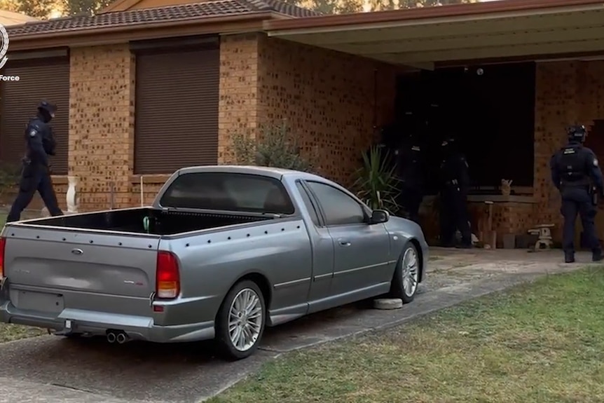  Car out the front of a house with police at the door.