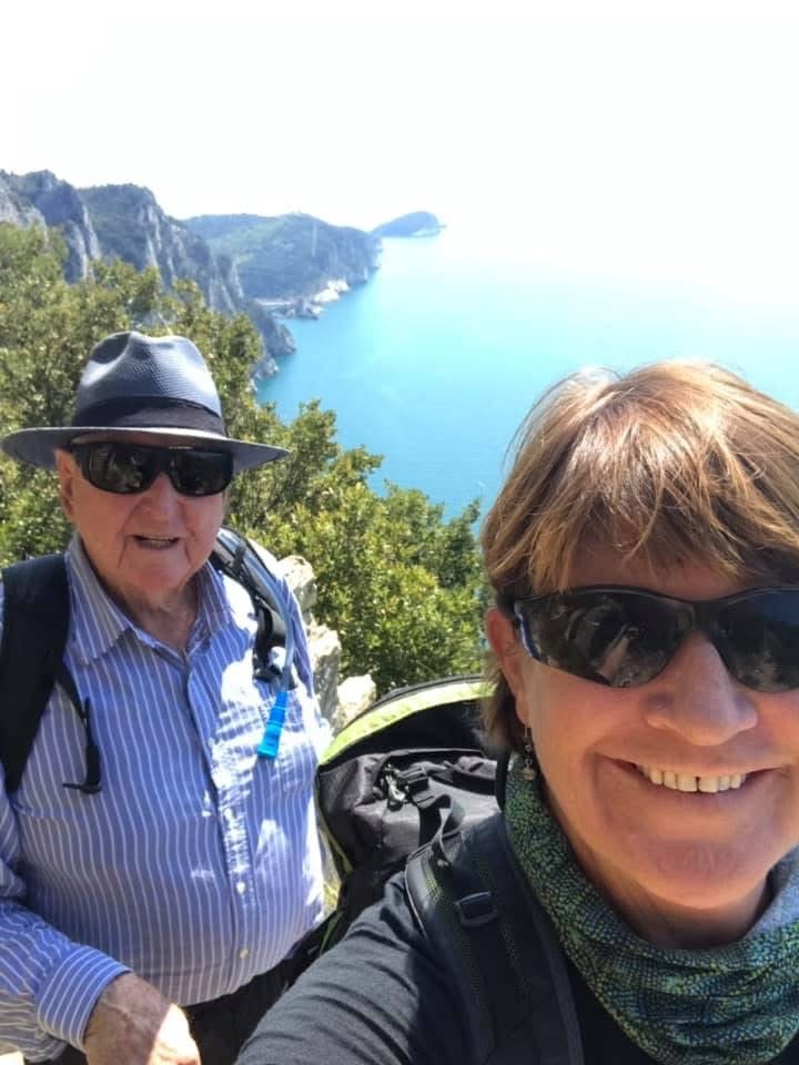 A man and a woman in hiking gear smiling into the camera in front of a lookout.