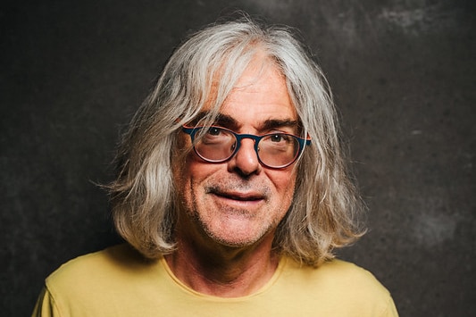 David Walsh smiles as he poses for a portrait. He's wearing a bright shirt with a geometric pattern