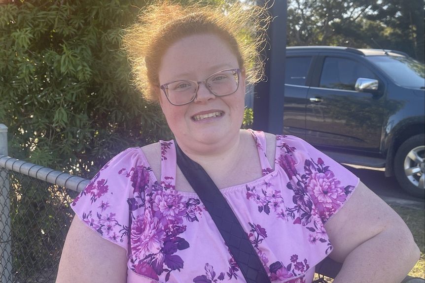 A woman with orange hair smiling with a sign in the background