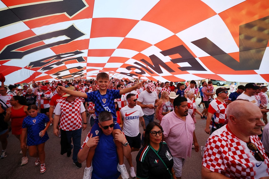 a parade of croatian fans walking under a giant red and white checkered flag