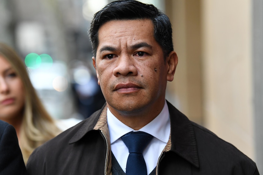 A man with dark hair looks serious as he is photographed outside court.