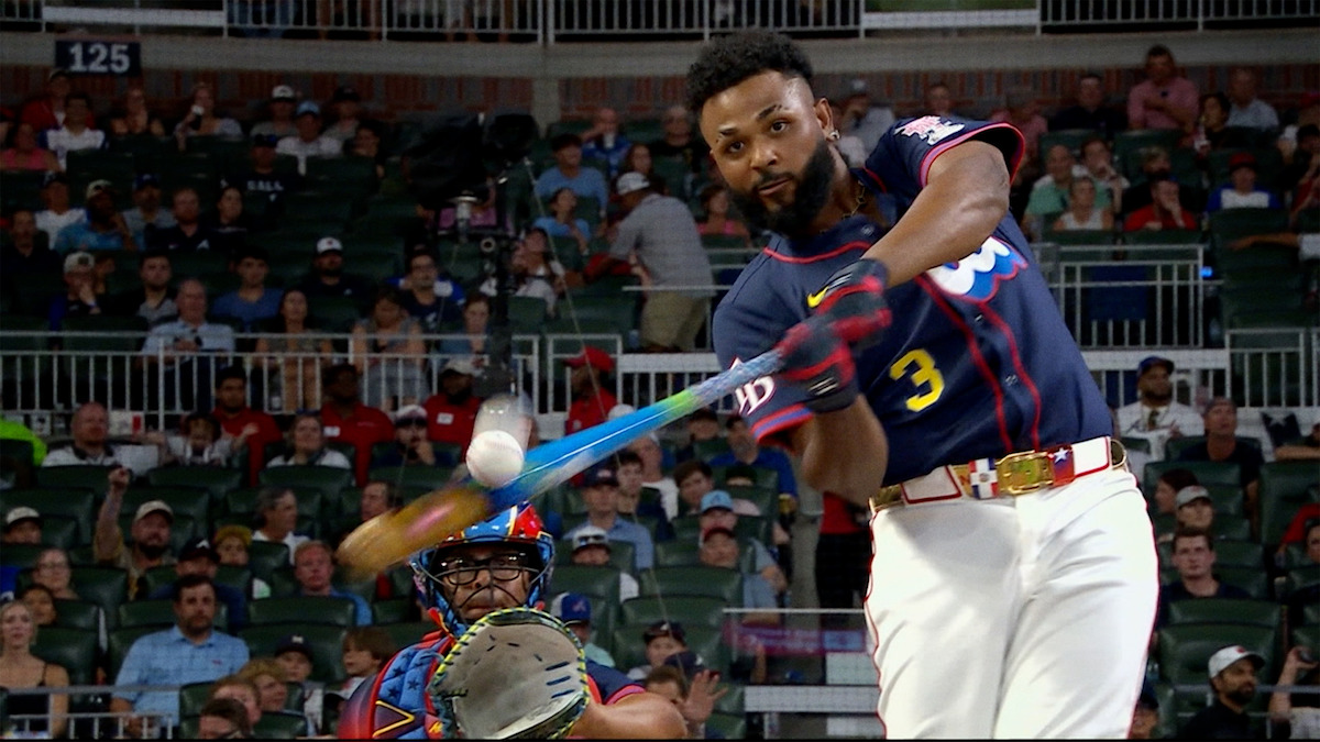 Baseball player in blue jersey swinging bat and hitting ball during a game, with a catcher and crowd in the stadium background, under stadium lights.