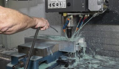 A technician is using a machine to drill pieces of silver metal; there is a light blue liquid coming out of jets next to the drill.
