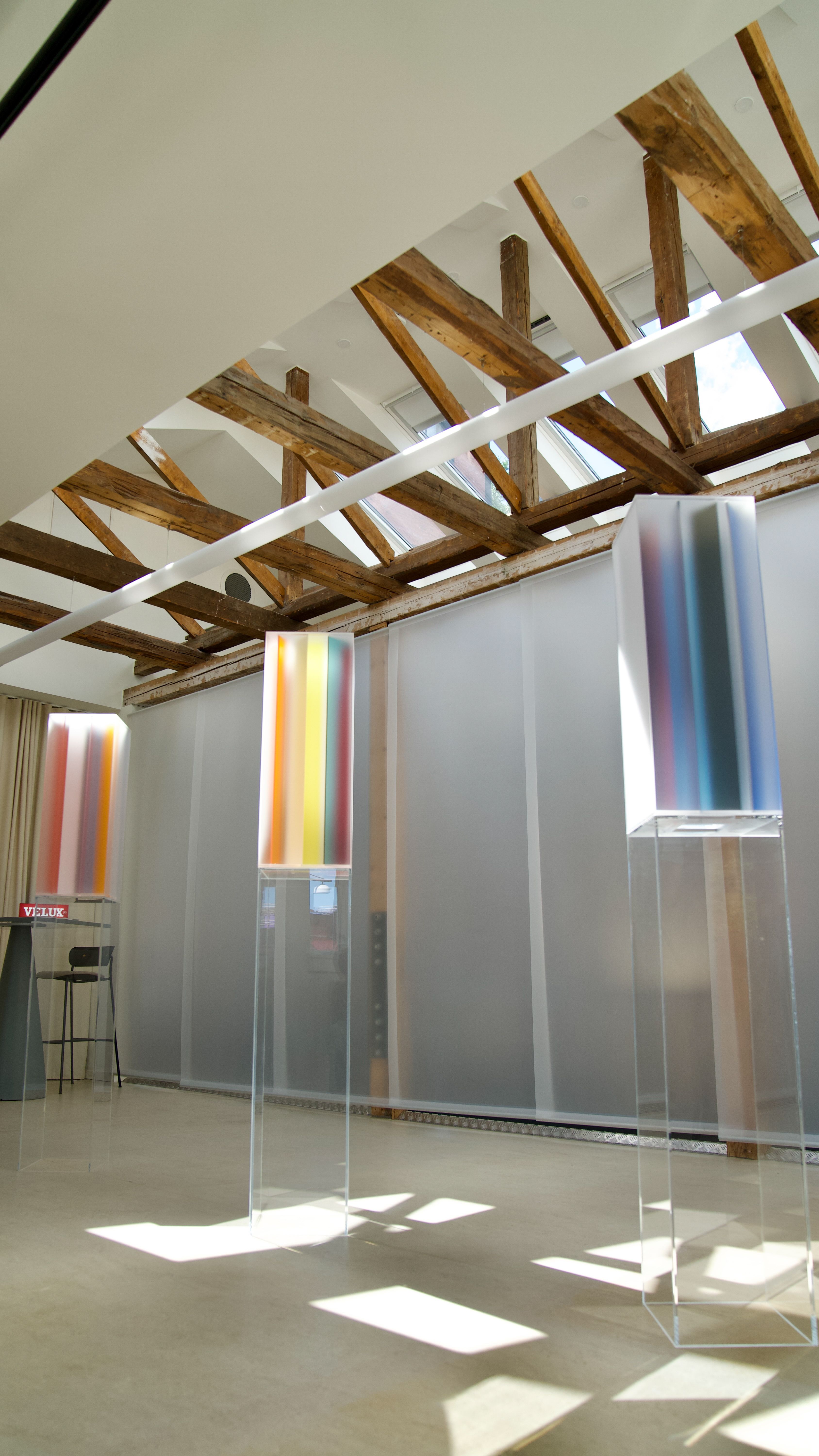 Installation view of an exhibition featuring gradient sculptural pieces made of opaque glass in different tones, placed atop transparent pedestals.