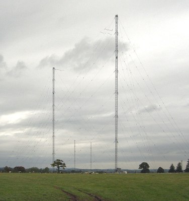 A pair of very large transmitting masts against a cloudy grey sky.