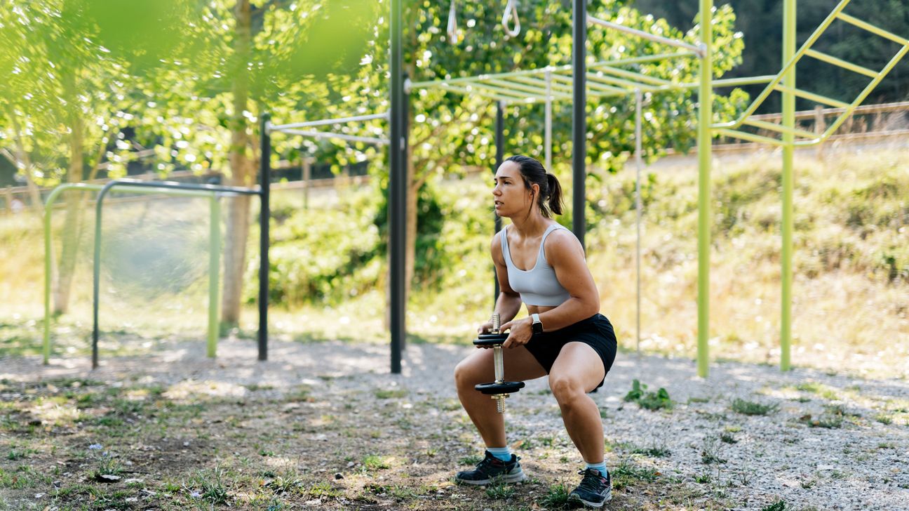 Female doing squats with a dumbbell in a park