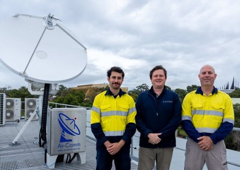 Three men standing next to a satellite dish installed on a rooftop