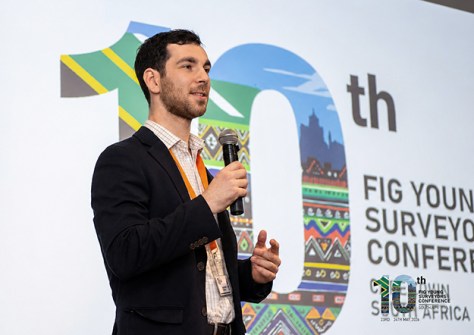 A man holding a microphone, standing on a stage, making a presentation during the Young Surveyors conference