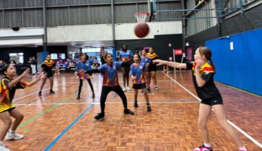 Primary school boys and girl students dressed in sporting attire and playing basketball on an indoor court