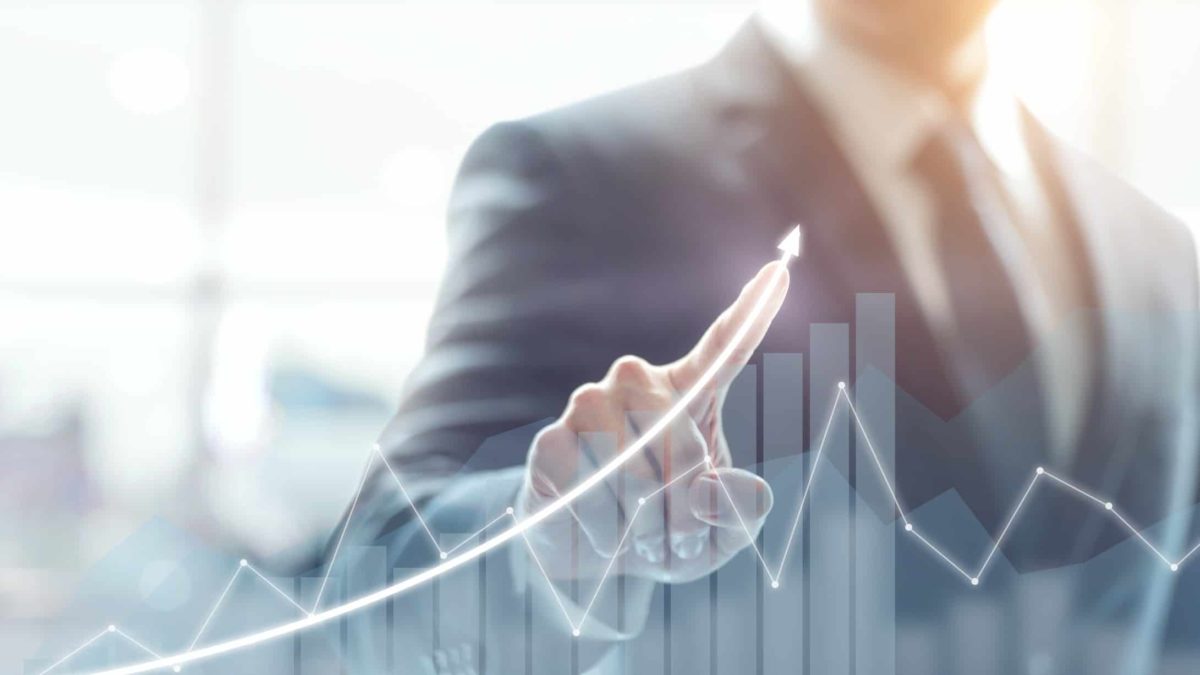 A business person directs a pointed finger upwards on a rising arrow on a bar graph.