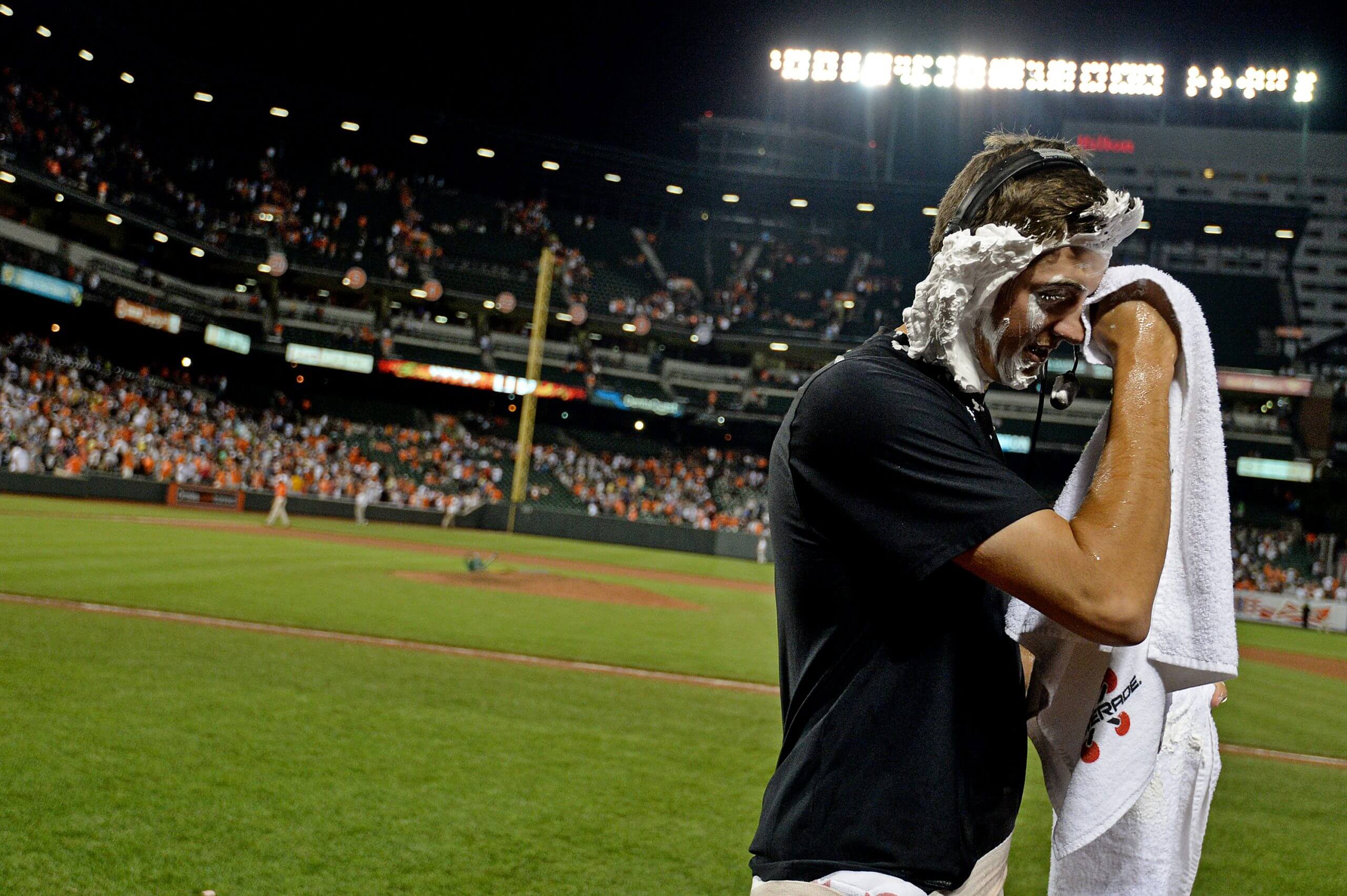 Kevin Gausman wipes having cream off his face as celebrates his first major-league win as a Baltimore Oriole, with the nighttime crowd in the background.