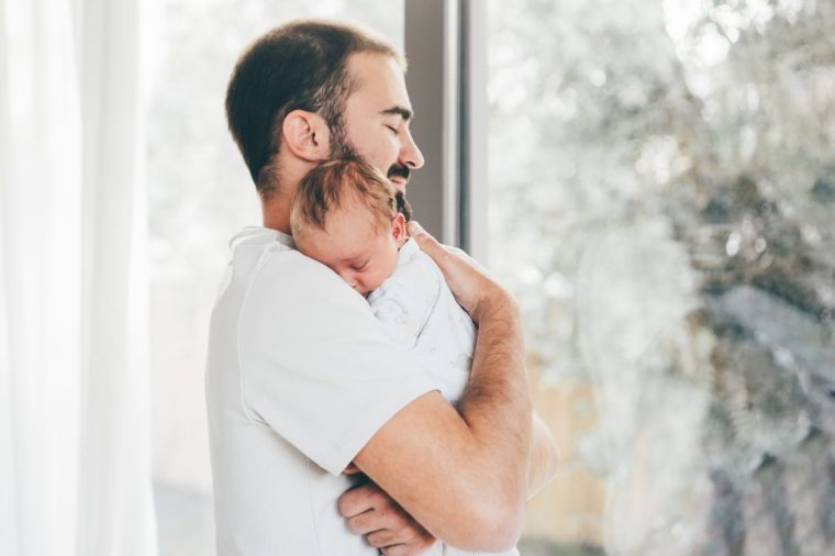 Father with baby on hands standing near window at home. - stock photo