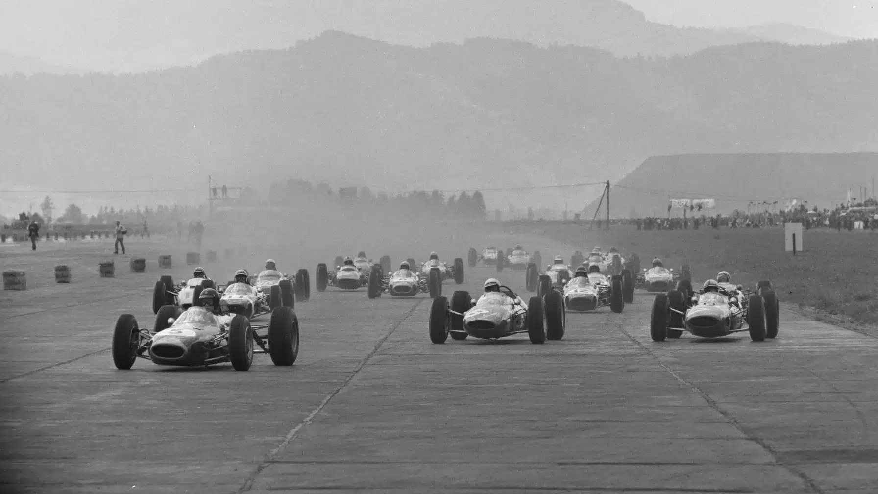 1964 Formula 1 Austrian GP, Zeltweg Airfield: Dan Gurney, Brabham BT7 Climax, leads Lorenzo Bandini, Ferrari 156 Aero, John Surtees, Ferrari 158, Jochen Rindt, Brabham BT11 BRM, and the rest of the field at the start