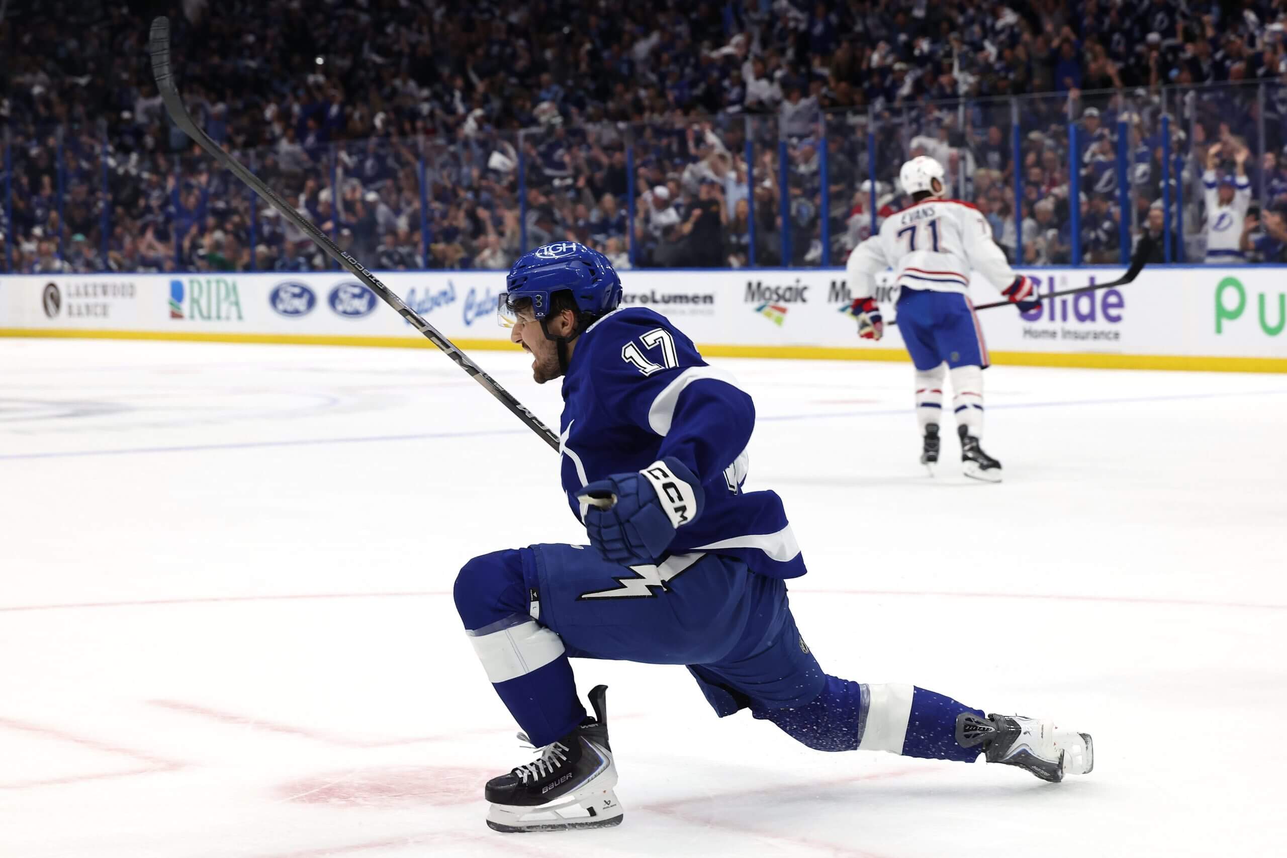 Dominic James slides on one knee celebrating after a goal for the Lightning, with a Canadiens player skating off in the distance.