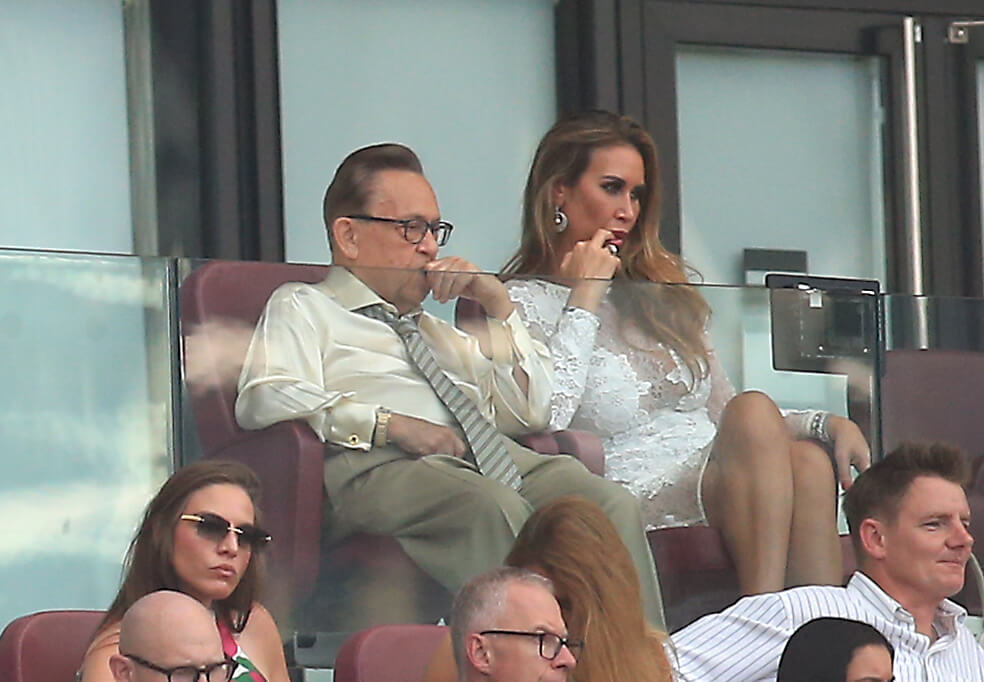 A man and a woman dressed in beige watch a football match