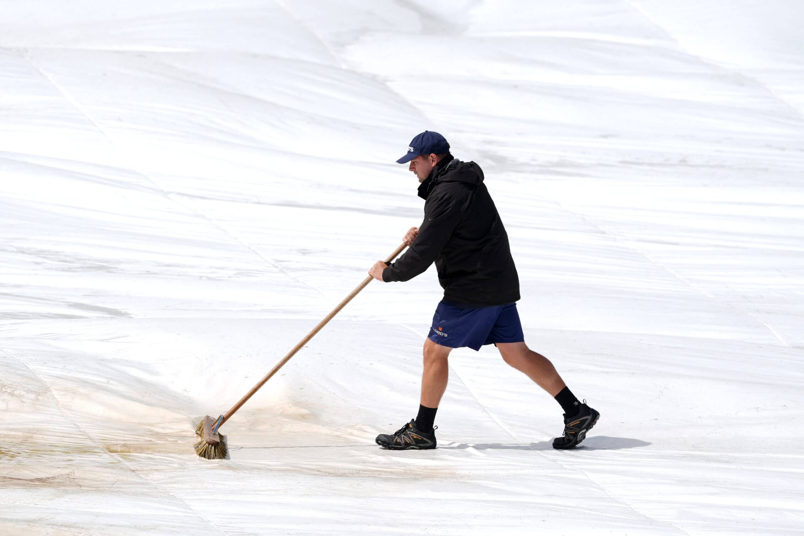 Ground staff sweep water off the rain covers