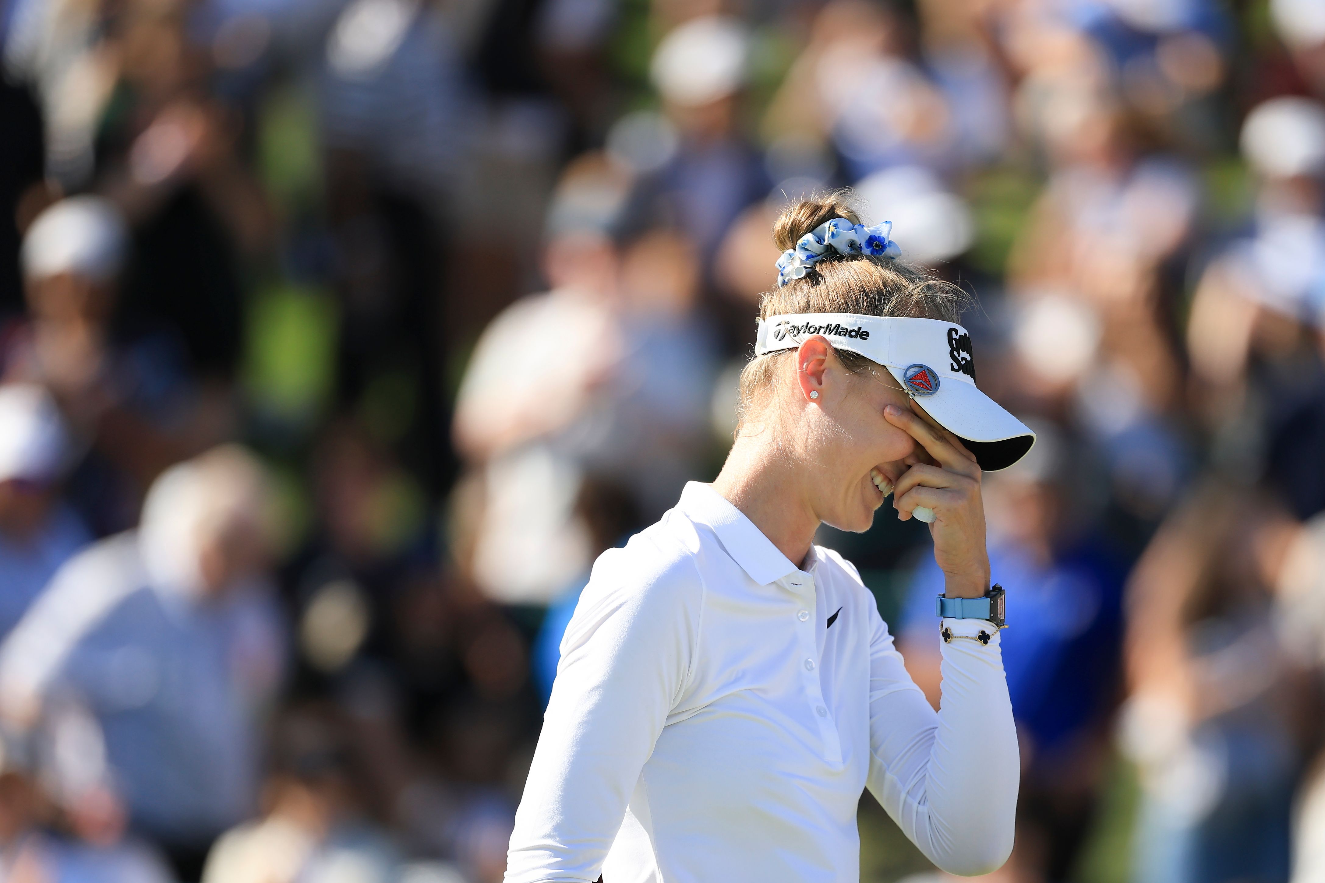 A woman golfer in a white visor looks down, appearing disappointed on the course.