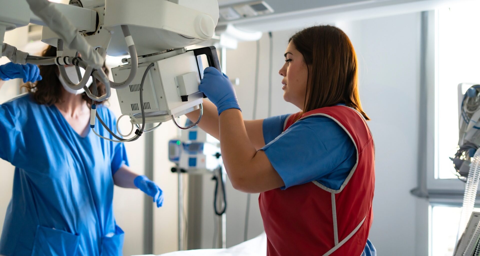 Two healthcare workers preparing a mobile x-ray machine in a hospital room