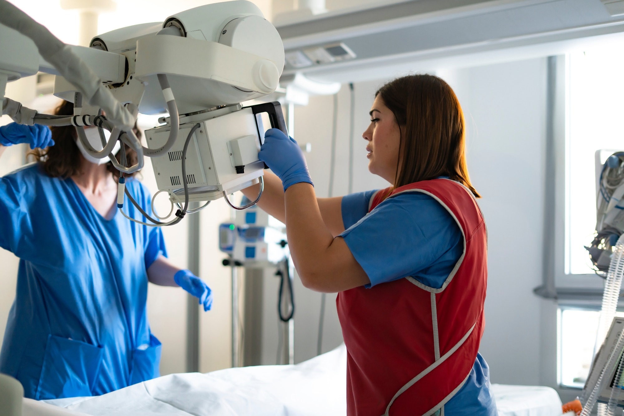 Two healthcare workers preparing a mobile x-ray machine in a hospital room