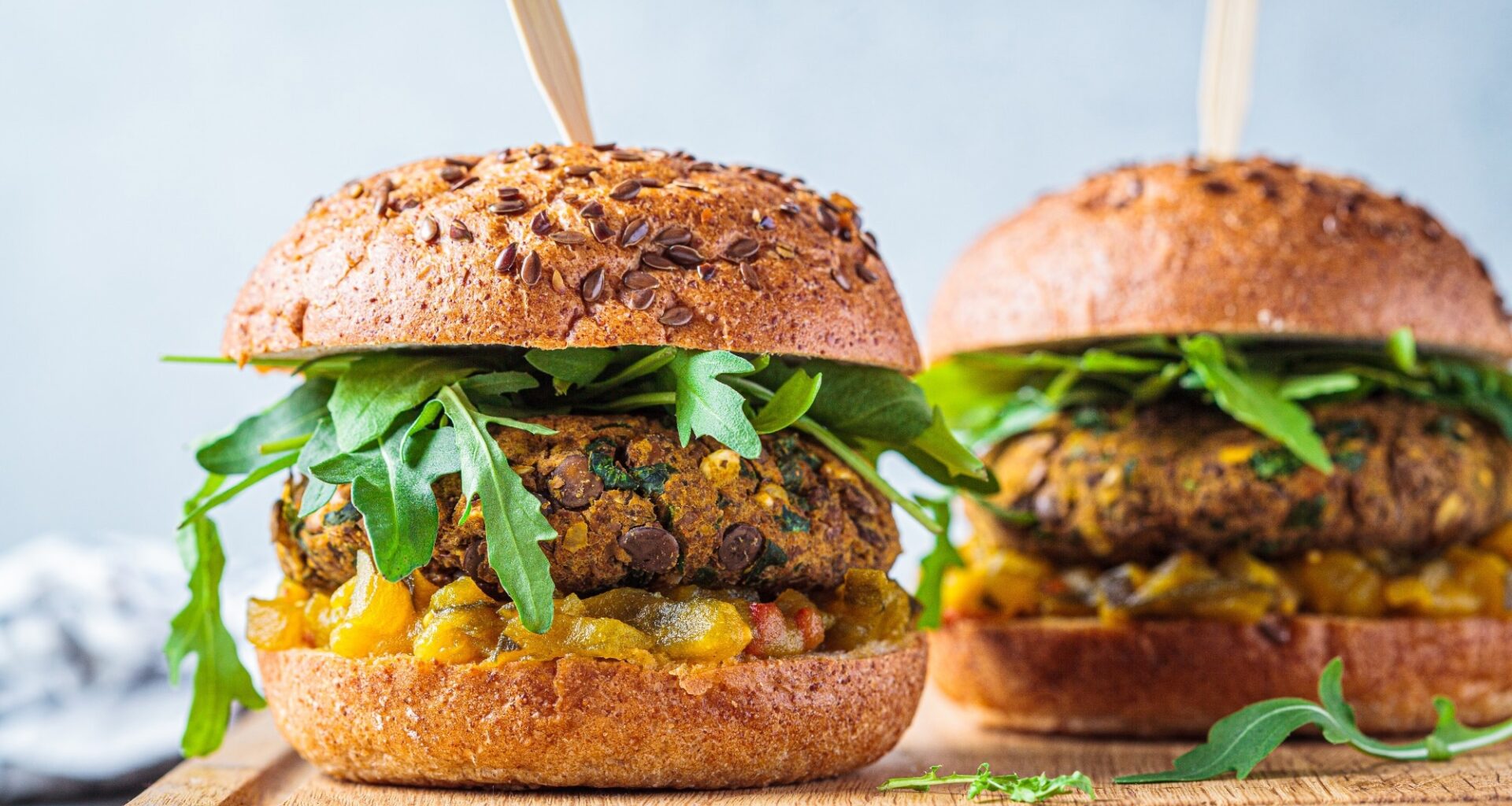 Vegan lentil burger with arugula, mustard sauce, fresh vegetables and sweet potato fries on a wooden board. Vegan food concept.