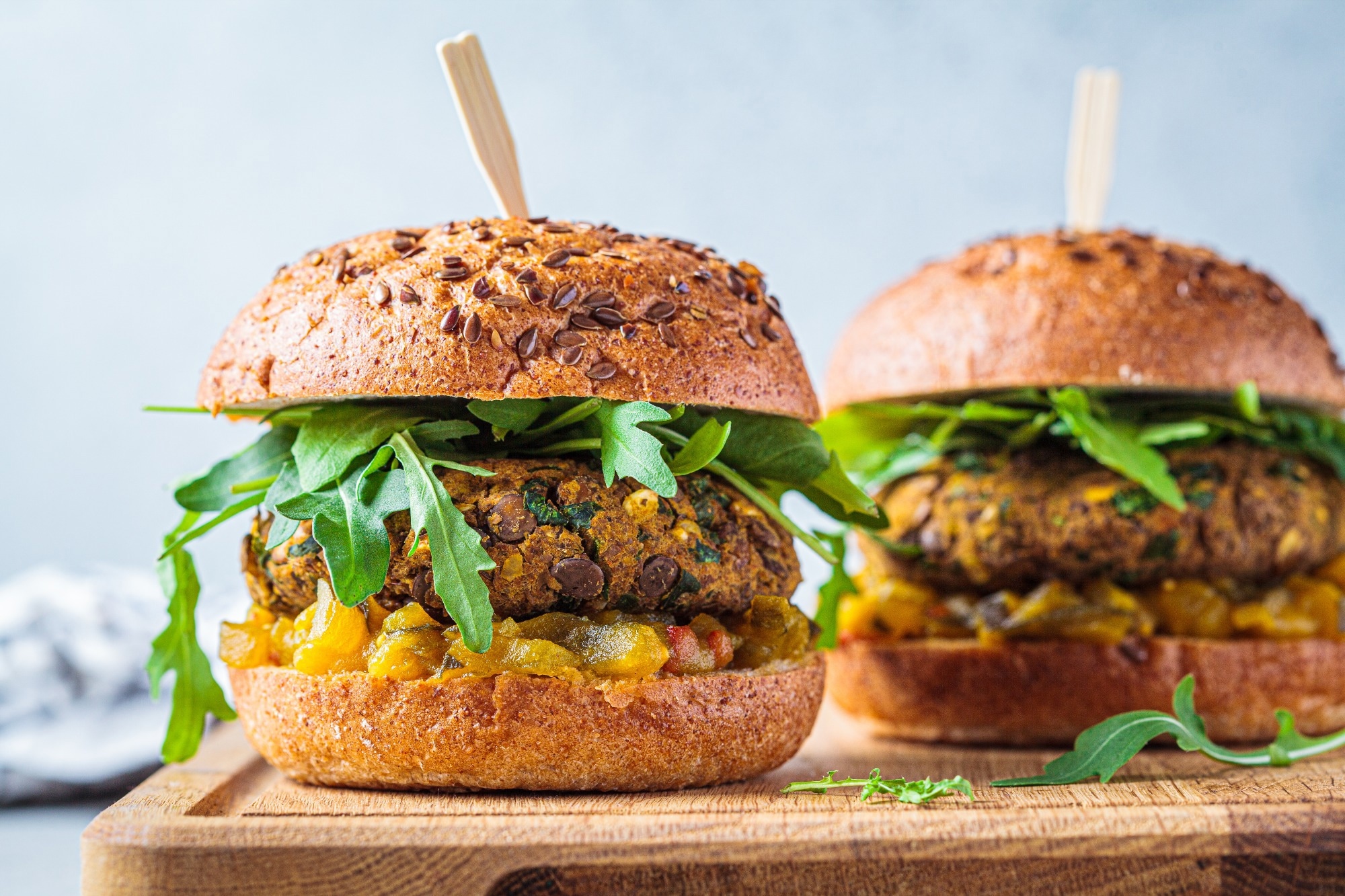 Vegan lentil burger with arugula, mustard sauce, fresh vegetables and sweet potato fries on a wooden board. Vegan food concept.