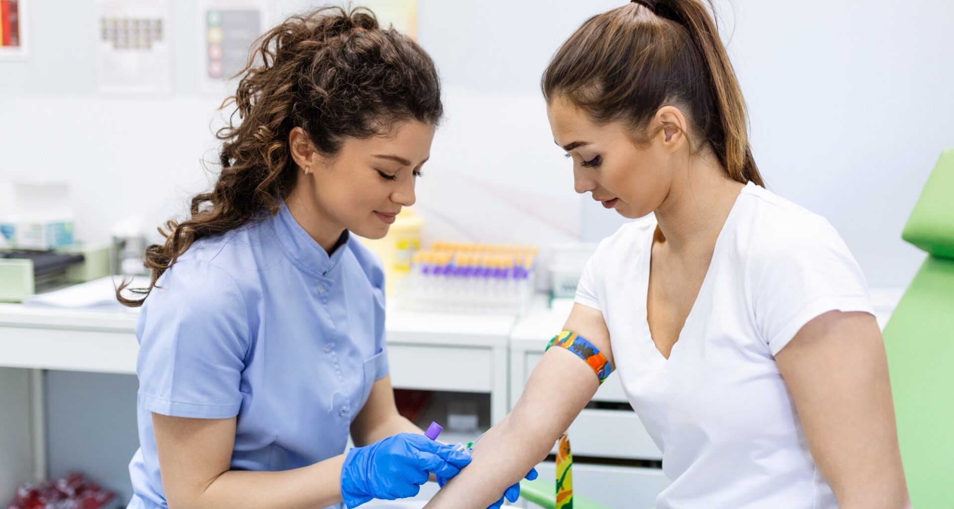 Preparation for blood test with pretty young woman by female doctor medical uniform on the table in white bright room. Nurse pierces the patient