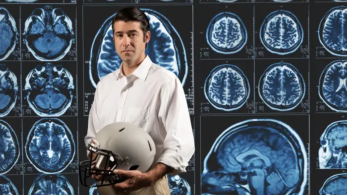 Brad Mahon holding helmet standing in front of MRI scans