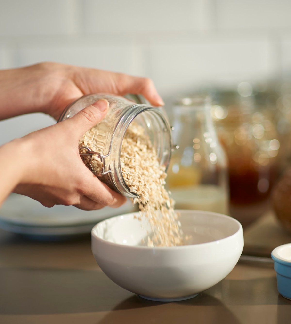 Close up of a woman preparing a wholesome breakfast by pouring oats into a bowl from a plastic free jar with fresh berries.